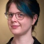 A slightly old photo of Molly de Blanc, in which she has blue highlights in her hair. She is wearing a black shirt and clear glasses.